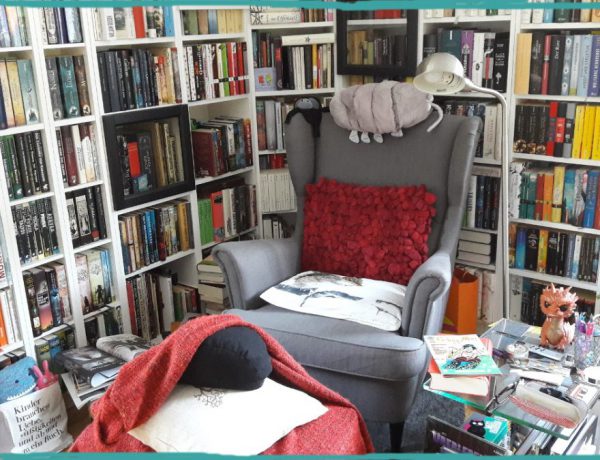 Bild einer Leseecke mit grauem Ohrensessel, Kissen, Decke und runherum weiße gefüllte Bücherregale