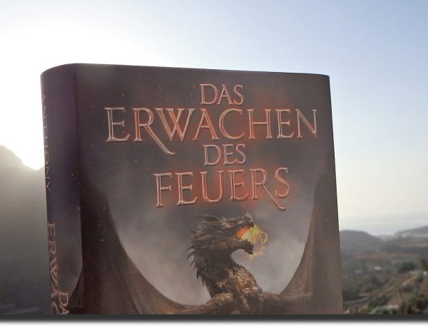 Buchcover vor einer Berglandschaft. Cover zeigt einen feuerspeienden Drachen.