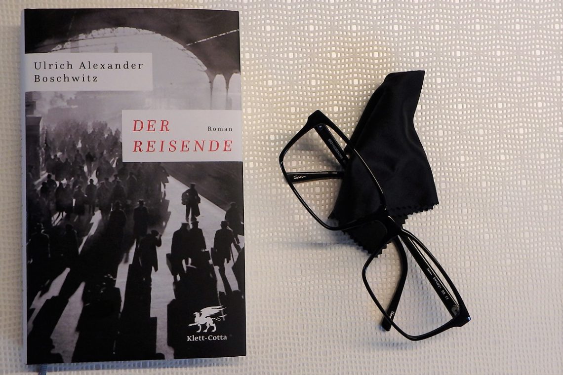 Buch liegt neben einer schwarzen Brille und einem Tuch auf einem hellen Untergrund