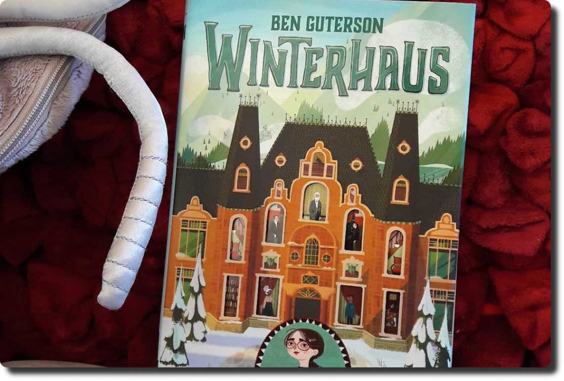 Winterhaus Cover - Buch liegt auf einem Kissen. Auf dem Cover ist das altmodische Hotel mit Einblick in viele Fenster