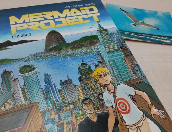 Mermaid Project 3 - der Comic liegt neben einer alten Postkarte mit einer Möwe über dem Meer