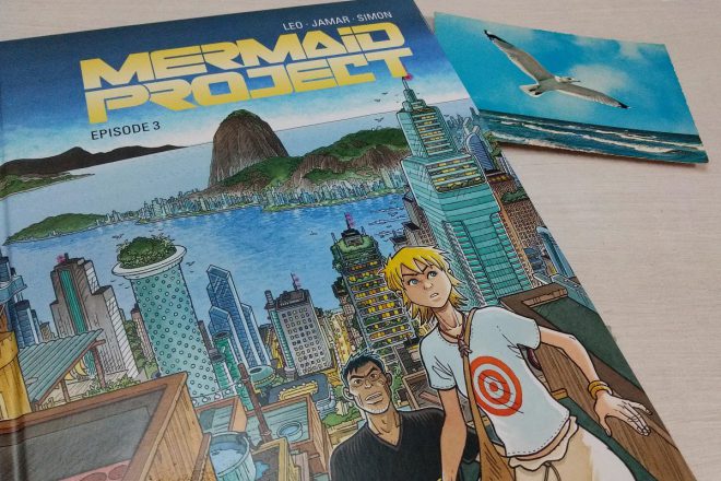 Mermaid Project 3 - der Comic liegt neben einer alten Postkarte mit einer Möwe über dem Meer