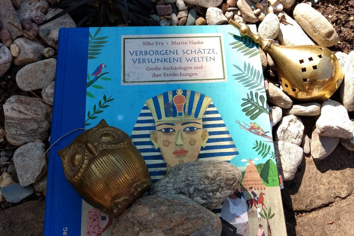 Buch auf dem ein Pharao abgebildet ist, darauf Steine, daneben ein glänzendes Artefakt
