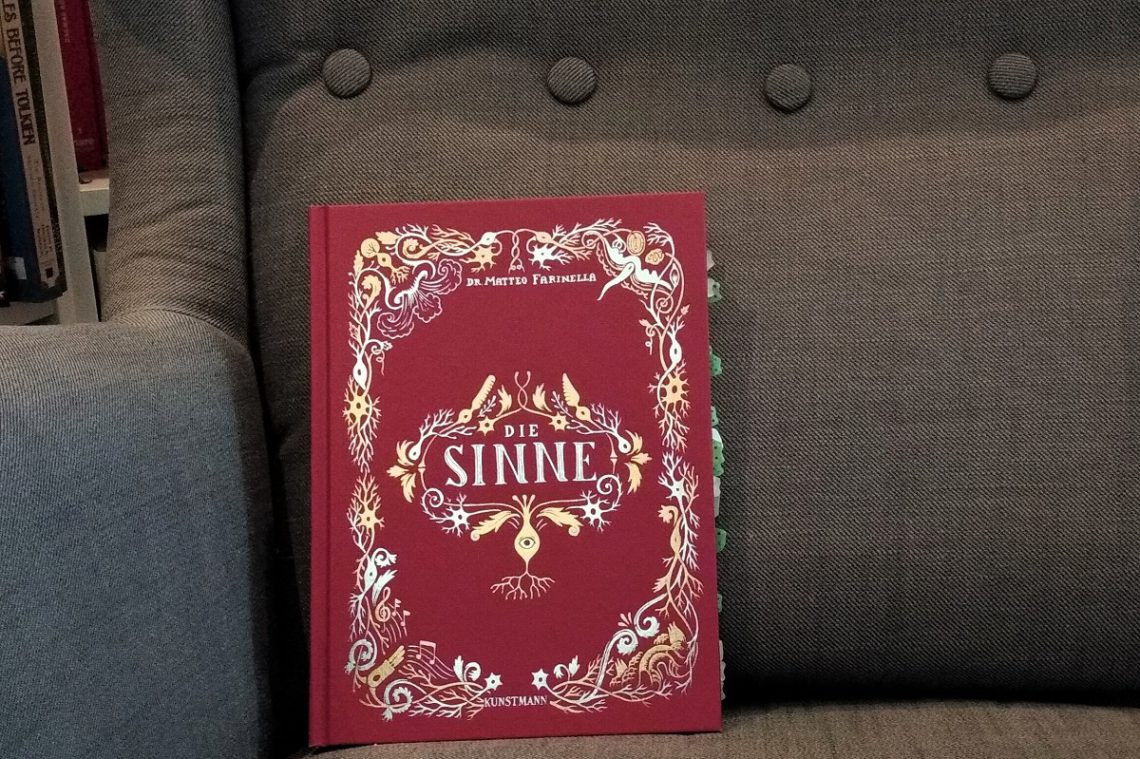 Rotes Buch mit goldenen Intarsien auf grauem Sessel