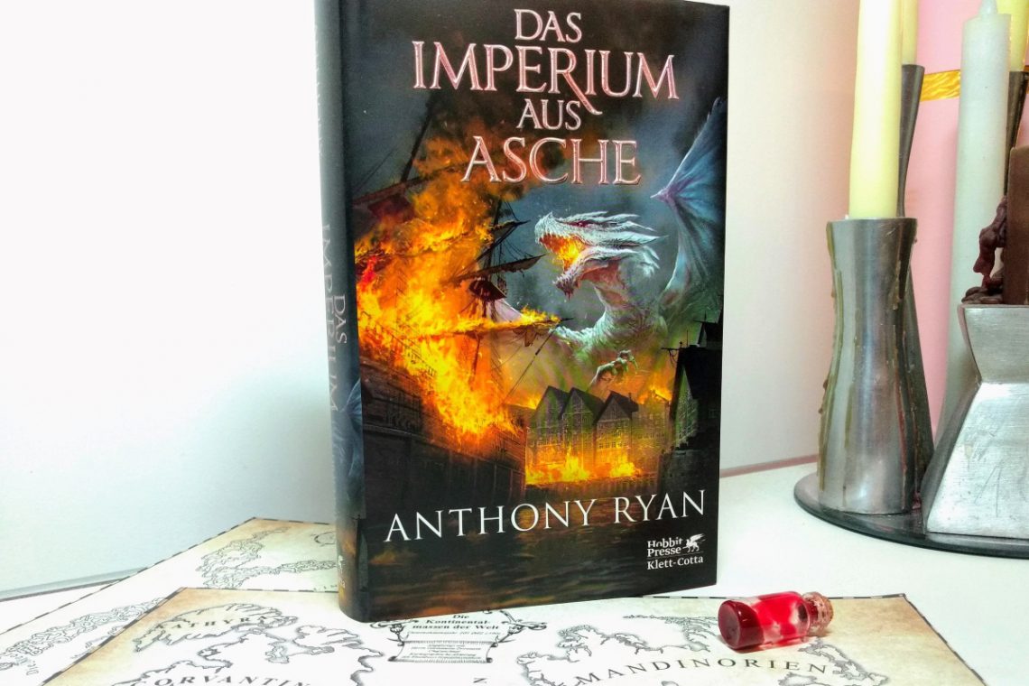 Buch mit feuerspeiendem Drachen auf dem Cover vor weißem Hintergrund, darunter eine Karte, daneben Kerzen