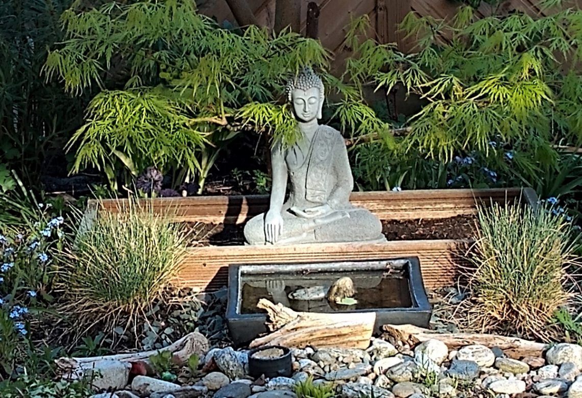 Buddha im Garten davor ein kleines Wasserbecken