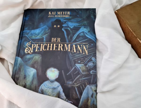 Comic vor einem hellen Tuch und daneben ein altes Buch