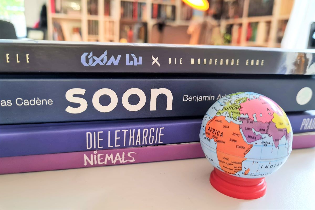 Vier Comics auf einem Stapel davor ein kleiner Globus im Hintergrund ein Bücherregal