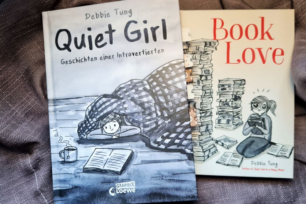 Quiet Girl auf dem ein Bettdeckendrache liegt und in dem versteckt sich eine junge Frau, daneben ein Buch und eine Tasse . Dann noch das Cover von Book Love, ein anderer Comic von Debbie Tung