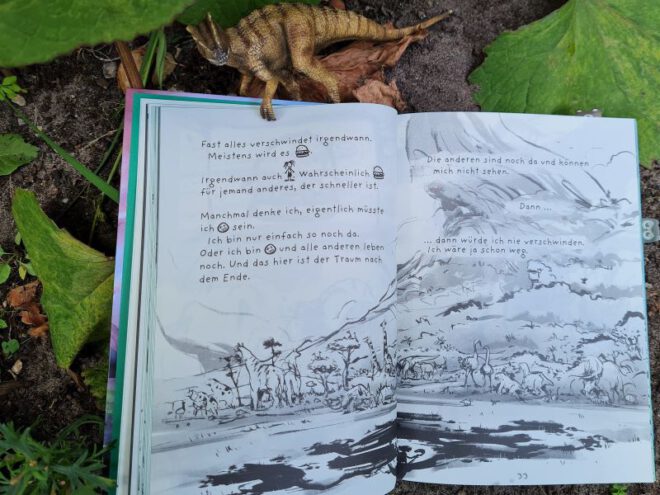 Geöffnetes Buch zeigt Zeichnungen und etwas Text, darüber ein Dinosaurier
