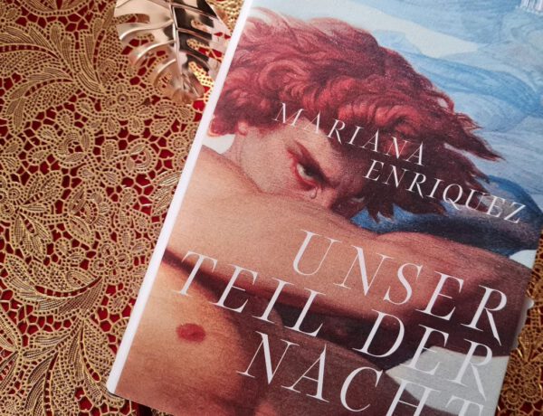 Roman Unser Teil der Nacht von Mariana Enriquez liegt auf einem goldenen Untergrund mit Spitzenoptik. Auf dem Cover ein rothaariger Mann mit freiem Oberkörper, der einen Arm vor ein Gesicht hält