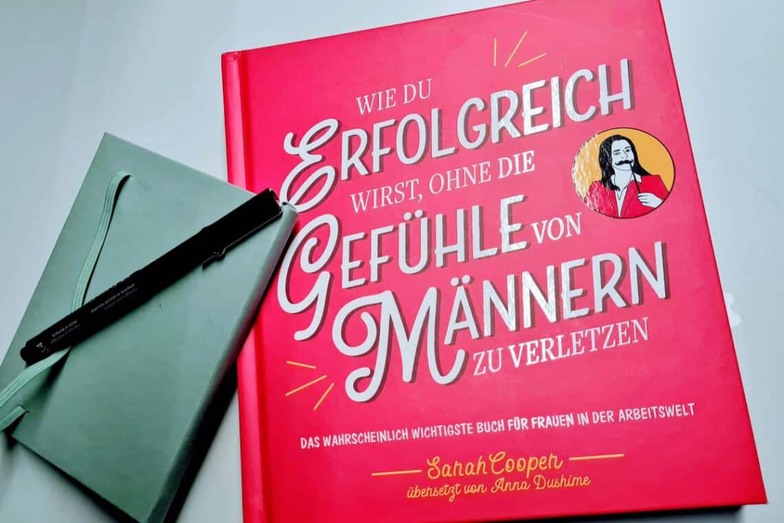 Pinkes Buch mit großer Titelaufschrift, daneben ein Notizbuch und ein schwarzer Stift