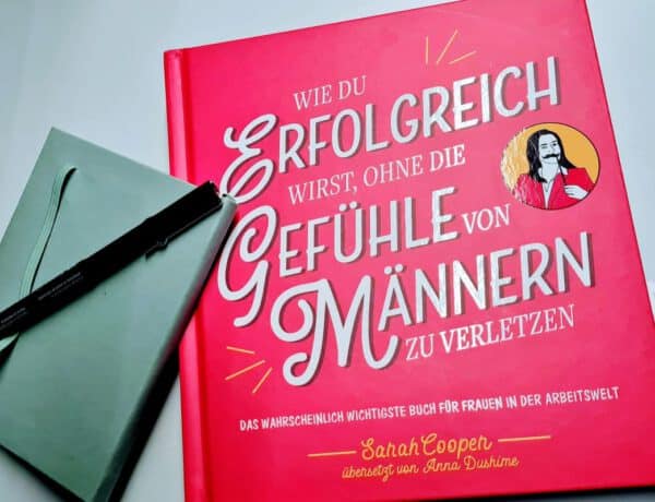 Pinkes Buch mit großer Titelaufschrift, daneben ein Notizbuch und ein schwarzer Stift