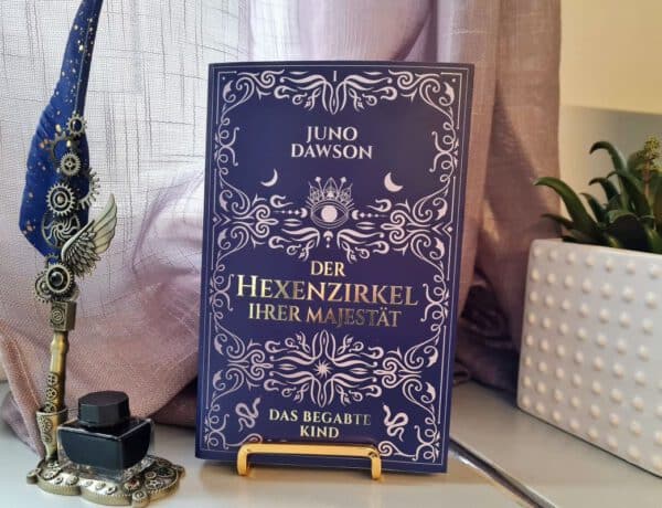 Buch mit Aufschrift Der Hexenzirkel Ihrer Majestät steht neben einer Schreibfeder und einem Tintenglas und einem Blumetopf mit Grünpflanze