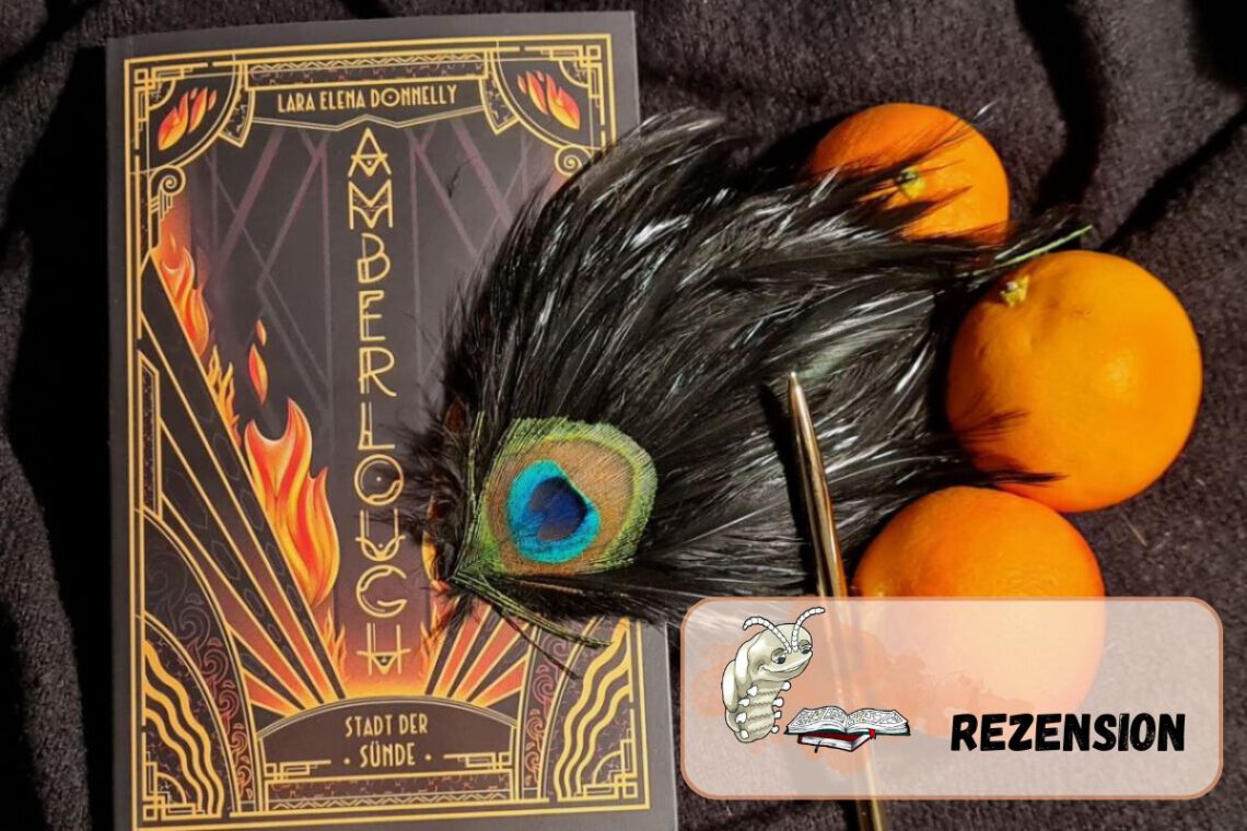 Buch in schwarz-orange mit Titel vertikal vorne liegt auf Wolluntergrund und daneben drei Orangen, ein goldener Stift und eine Pfauenfeder