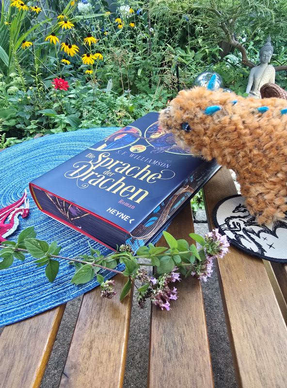 Buch liegt auf einem Tisch im Garten, daneben ein Plüschdrache