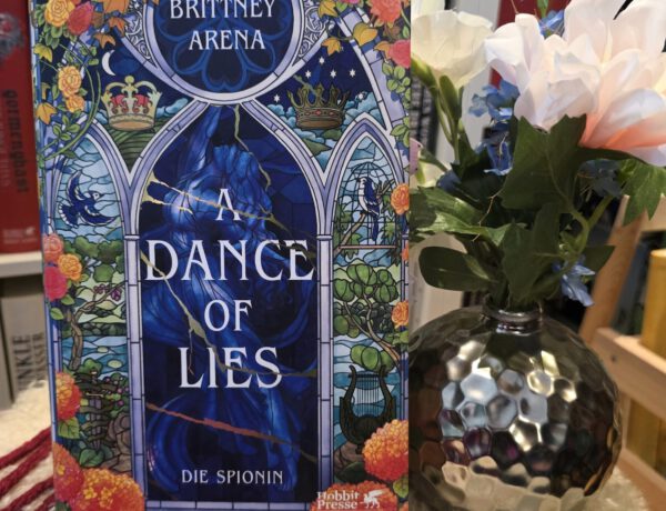 Buch steht vor einem Regal, daneben eine silberne runde Vase mit Blumen