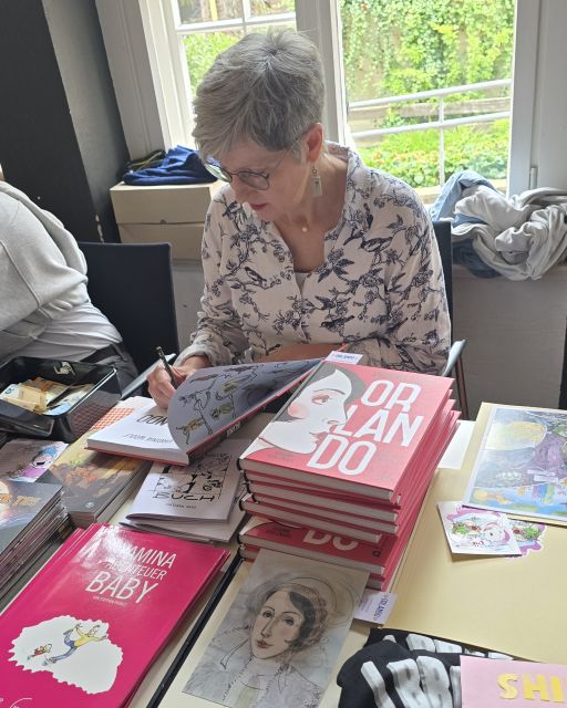Frau signiert in einem Comic, daneben Stapel mit Comics